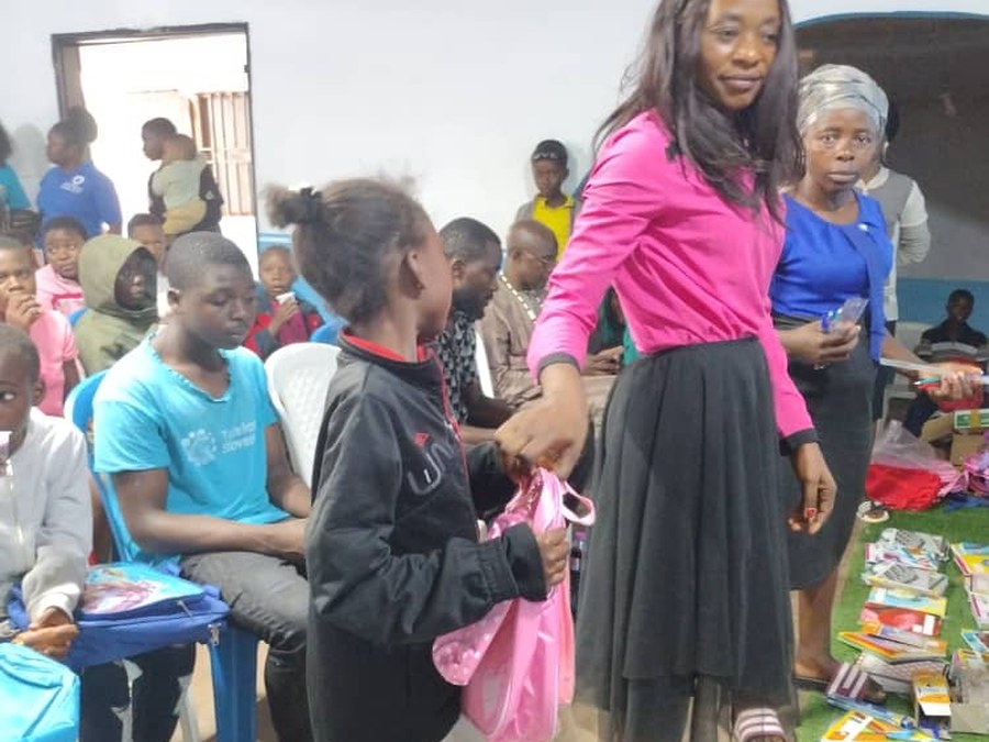 COHEC volunteer handing a pink backpack to a child